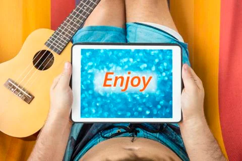 Young man lying on a hammock with tablet device looking at  blurred blue back Stock Photos