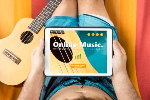 Young man lying on a hammock visiting an online music website with tablet dev Stock Photos