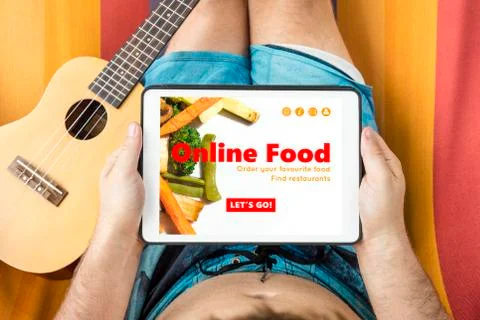 Young man lying on a hammock visiting an online food website with tablet devi Stock Photos