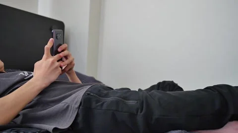 The young man lying on his bed is busy on the phone Stock Footage 270314305