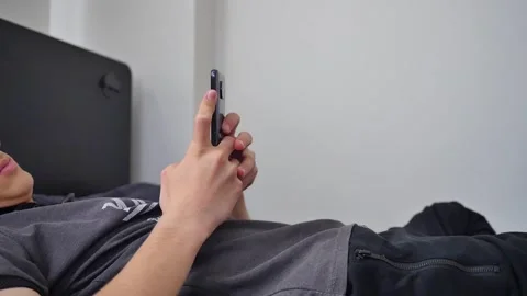The young man lying on his bed is busy on the phone Vídeos de archivo 270314622