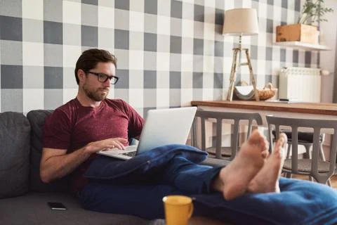 Young man lying on his sofa using a laptop Stock Photos