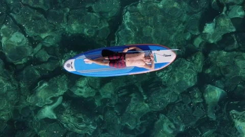 Young man lying on a paddleboard at turquoise sea close to the big cliffs Stock Footage 146640003