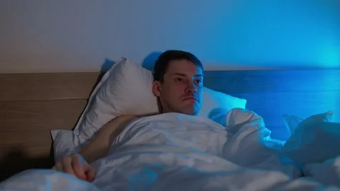 Young man lying on pillow under blanket and sleeping on bed in late evening Stock Footage 163803051