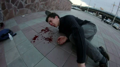 Young man lying on the sidewalk. He's bleeding from the nose Stock Footage 69789288
