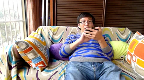 Young man lying in the sofa and playing smartphone games, finally win a victory Stock Footage 36457392