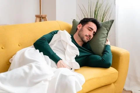 Young man lying on sofa and sleeping in cozy living room at home Stock Photos