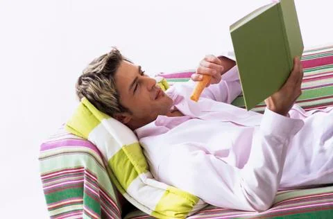 Young man lying on sofa, reading book, side view Stock Photos