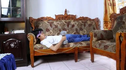 Young man lying on the sofa while lifting dumbbells. lazy and tired of exerci 스톡 사진