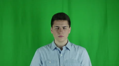 Young man is mad and sighs in front of a greenscreen in a blue shirt Vidéo 59082968