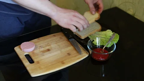 The young man makes himself a tasty and juicy sandwich from two pieces of bread, Stock Footage 112684430