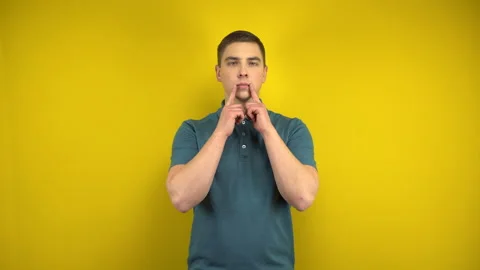 A young man makes a sad smile on her face with his fingers on a yellow Stock Footage 143391582