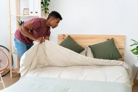 Young man making the bed in his room. Stock Photos