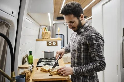 Young man making breakfast in tiny kitchen at trailer van and cutting sandwiches Stock Photos