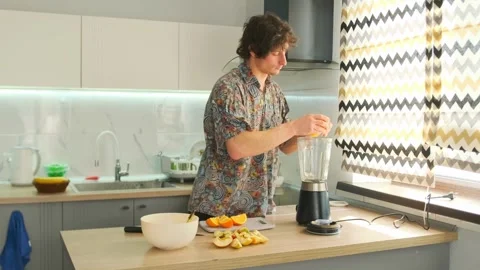 Young man making healthy orange smoothie in home kitchen Stock Footage 311809249