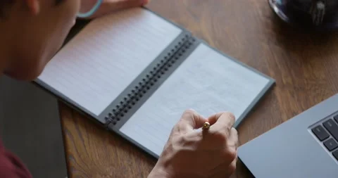 Young man making notes in paper notebook with a ballpen.Guy sitting at wooden Stock Footage 164600620