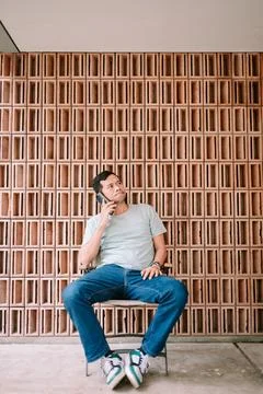 Young man making a phone call, looking thoughtful by brick wall Stock Photos