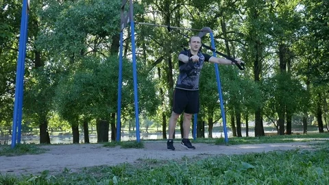 Young man making push-up exercises on fitness loops in a summer park. 4K slow Stock Footage 98446335