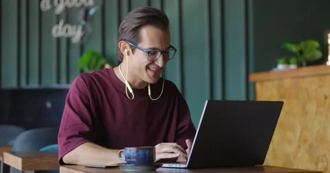 Young man making a video call via laptop while sitting in coffee shop Video stock 163996647