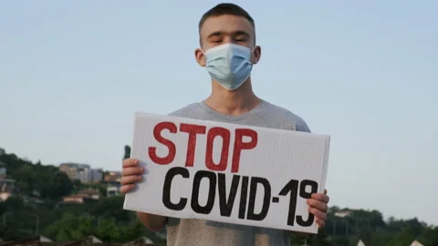 Young man in mask protestant stands with sign Stop Covid-19 on cardboard Stock Footage 134050558