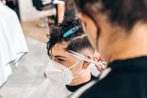 Young man with mask sitting while a woman cut his hair in a hairdresser Stock Photos