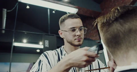A young man, a master barber mills a client in the salon. Video stock 139624221