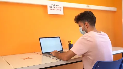 Young man with a medical mask working in the office with the computer maintai Stock Footage 133707553