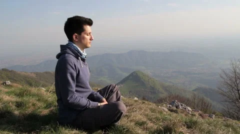 Young man meditates alone on the mountain, with views of the plain Stock Footage 49825744