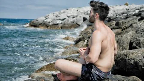Young Man Meditating or Doing Yoga Exercise by Sea Stock Photos