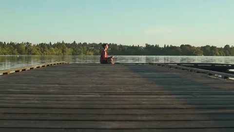 A young man meditating on a pier Stock Footage 76223294