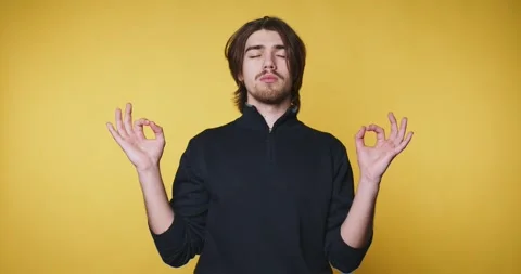 Young man is meditating with a serene expression on yellow background, embo.. Stock Footage 314336967
