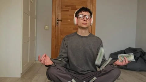 Young man meditating while listening to money meditation as dollar bills fall Stock Footage 303904655