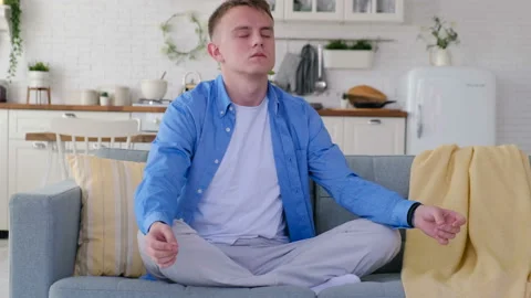 Young man meditating while sitting on a sofa Video stock 128252794