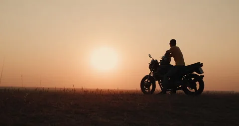 A young man meets the sunset while sitting on a motorcycle Stock Footage 156525007
