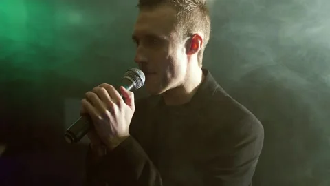 Young man with a microphone on a background of smoke in a dark room Stock Footage 105782715