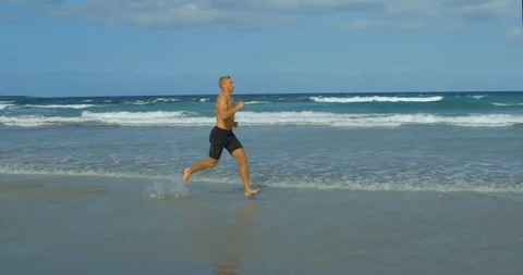 A Young Man in Mid 20's Running in Slow Motion Shirtless on a Beach. 스톡 동영상 85512696
