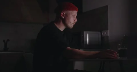 A young man, a millennial freelancer, sits down at work at night and drinks Stock Footage 302900484