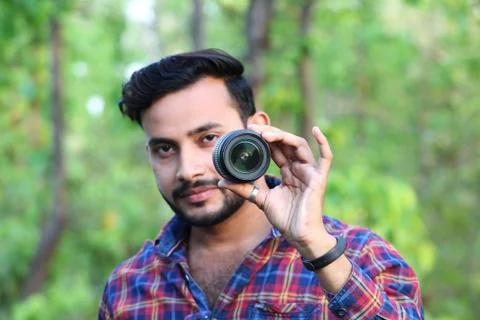 Young man model holding a camera lens in front of his face with focus Stock Photos