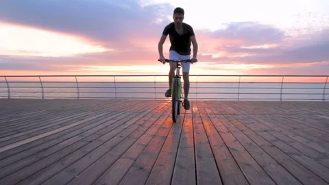 Young man with mountain bike on seafront during sunset or sunrise 動画素材 75772487