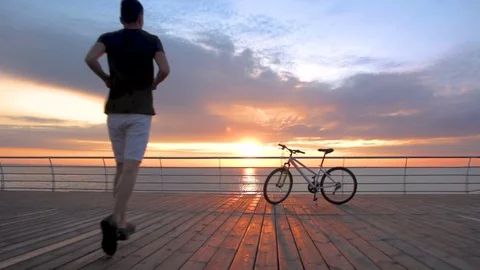 Young man with mountain bike on seafront during sunset or sunrise Vídeos de archivo 75773144