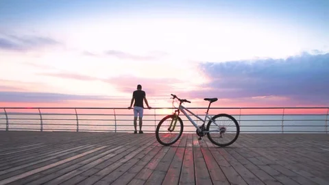 Young man with mountain bike on seafront during sunset or sunrise Vídeos de archivo 75961382