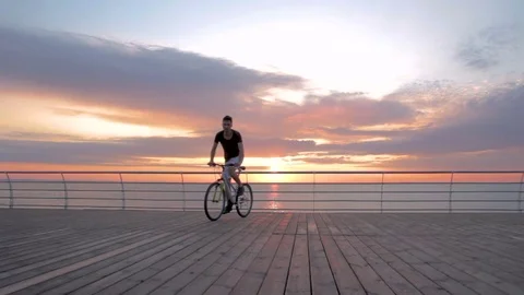 Young man with mountain bike on seafront during sunset or sunrise 動画素材 75965064