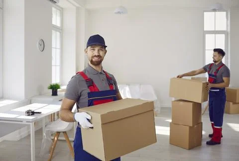 Young man mover worker in uniform holding a cardboard box and looking at camera Stock Photos