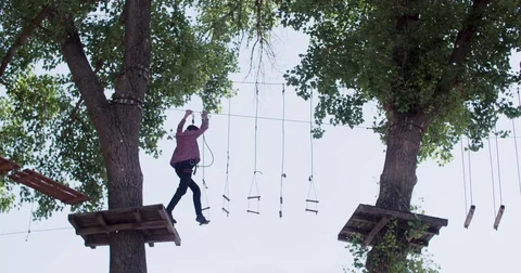 Young man moving on adventure rope park 4k video. Climber walks on ladder board Stock Footage 79238338