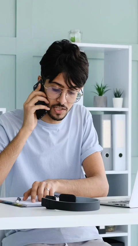 Young Man Multitasking on a Phone Call and Laptop at his Desk Stock Footage 328129165