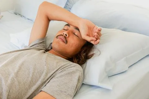 Young man with a mustache lying on a bed with his hand on his forehead, app.. Stock Photos
