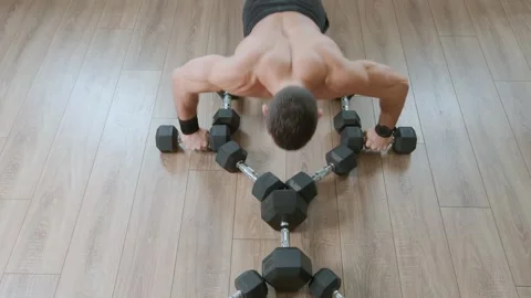 Young man with a naked torso does push-ups from dumbbells lying on floor and Vidéo 271024936