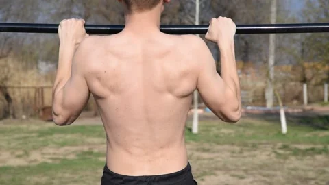 A young man with a naked torso pulls up on a horizontal bar on a sports field Stock Footage 131142971