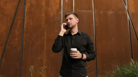 Young man near a rusty wall drink coffee and talk on the phone. Stock Footage 138992874
