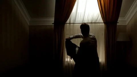 Young man near the window puts on a business jacket Stock Footage 106674629